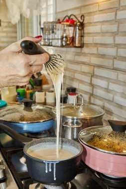 Chef stirs the bechamel sauce, which is cooked on gas stove, into saucepan.