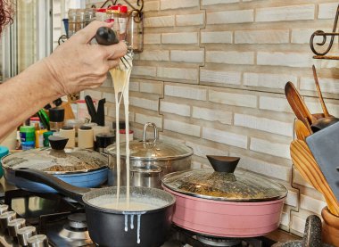 Chef stirs the bechamel sauce, which is cooked on gas stove, into saucepan.