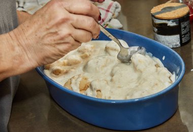 Chef pours bechamel sauce, cauliflower in ceramic dish for baking in the oven.