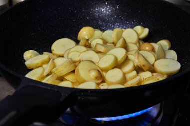 Sliced potatoes are fried in frying pan on gas stove.