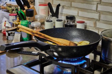 Sliced potatoes are fried in frying pan on gas stove.
