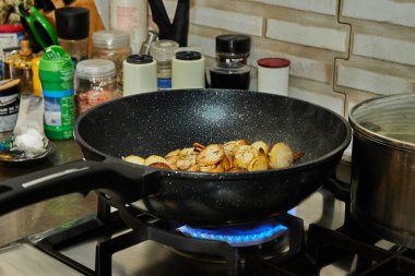 Sliced potatoes are fried in frying pan on gas stove.