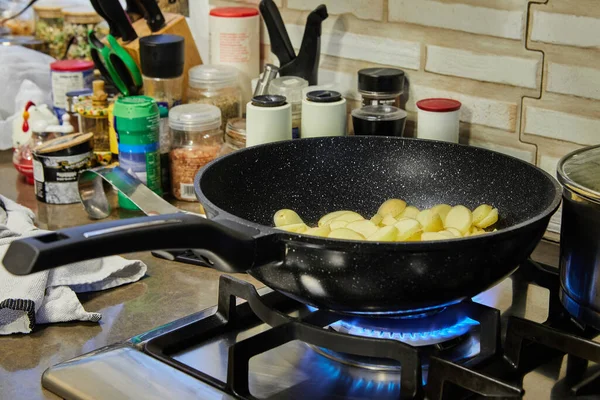 Sliced potatoes are fried in frying pan on gas stove.