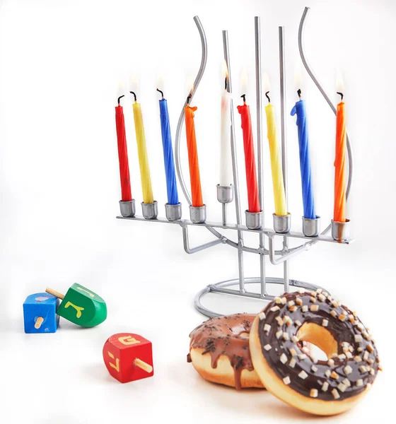 Jewish holiday Hanukkah background. Traditional dish is sweet donuts. Hanukkah table setting candlestick with candles and spinning tops on white background. Lighting Chanukah candles. Copy space.