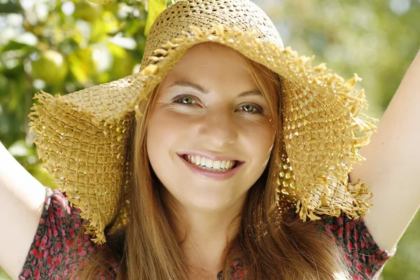 Glückliche junge Frau im Garten mit Strohhut — Stockfoto