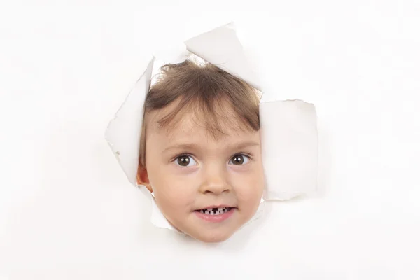 Little girl looks through a white paper wall — Stock Photo, Image