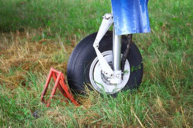 Siyah büyük uçak tekerleği yeşil çimlerin üzerinde duran kırmızı engelin üzerinde dinleniyor.