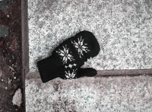 Черная шерстяная варежка с белым орнаментом, оставленная на мраморной лестнице на открытом воздухе — стоковое фото
