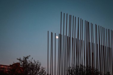 Küçük bulanık ay, inşaat alanı parmaklıkları ve ağaç kaplaması arasında mavi gökyüzünde neredeyse tam bir daire çiziyor.