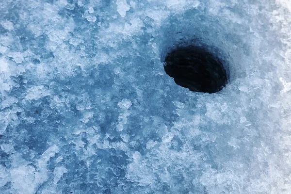 厚い湖の氷で作られた氷の釣りのための暗い丸い水の氷穴表面に硬い雪と — ストック写真