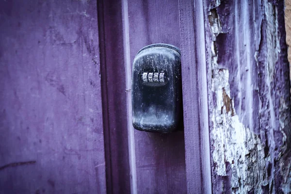 Old mechanical coded door lock on purple door and peeling plaster wall