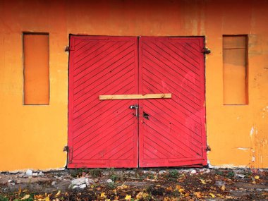 Parlak kırmızı ahşap garaj kapısı turuncu duvardaki çift giriş kapısı kilitlenmiş ve çivilenmiş.