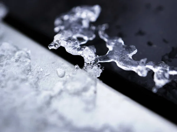 Melting snow forming an ice shape on a black and silver car surface background