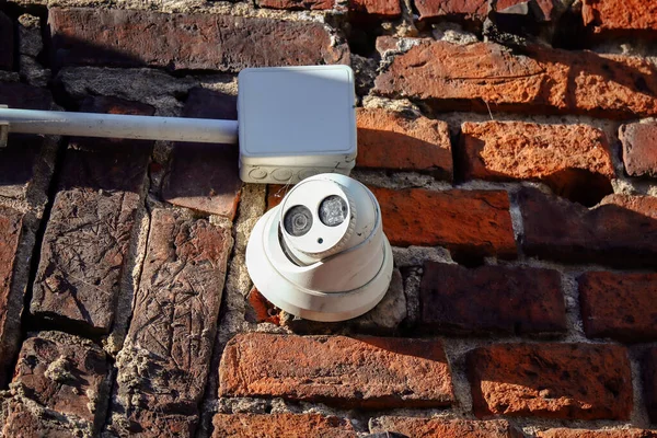 Spherical white video camera mounted on an old red brick wall in sun beams