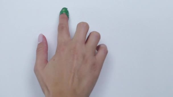 Uma mão com tinta verde no dedo desenha um sorriso sorridente em uma superfície branca. — Vídeo de Stock