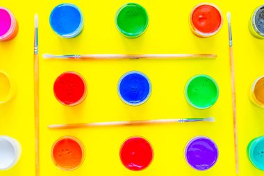 Görüntünün her yerinde çok renkli boya kutuları var. Sıraları sarı arkaplandaki boya fırçalarıyla ayrılmış. Üst görünüm, düz görünüm, kopyala boşluk, izole et.