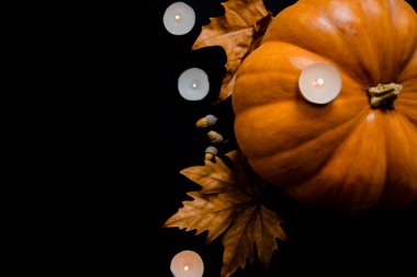 Siyah arka planda yaprakları, meşe palamutları ve mumları olan turuncu bir balkabağı..