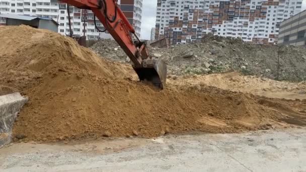 Grävmaskinerna orange skopa plockar upp sand från en stor sandhög. — Stockvideo
