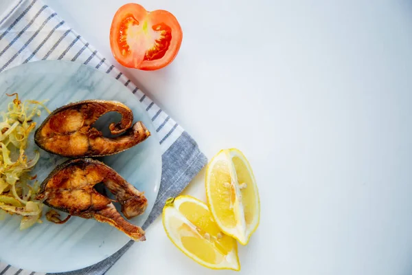 Soğanlı kızarmış balık tabakta, waffle havlusunda, limonlu ve domatesli beyaz arka planda..