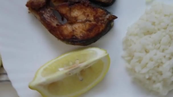 Smażona ryba z cebulą i ryżem jest na talerzu, na gofrowym ręczniku na białym tle. Zapis żywności kręcącej się w kółko. — Wideo stockowe