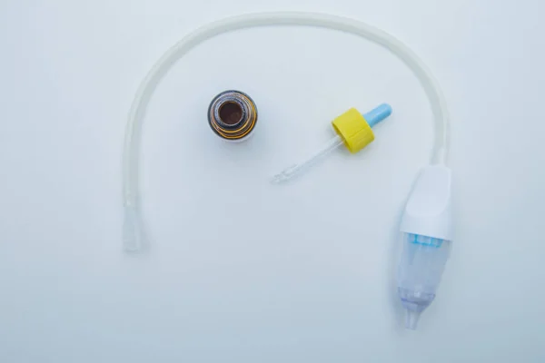 Çocuk aspiratörü beyaz arka planda yarı daire şeklinde uzanıyor, içinde pipetle akan bir burundan damlalar var.. 