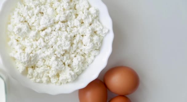 Un plato blanco con queso cottage gira, los huevos son visibles desde el lado, luego el queso, luego un vaso de leche sobre un fondo blanco. — Vídeos de Stock