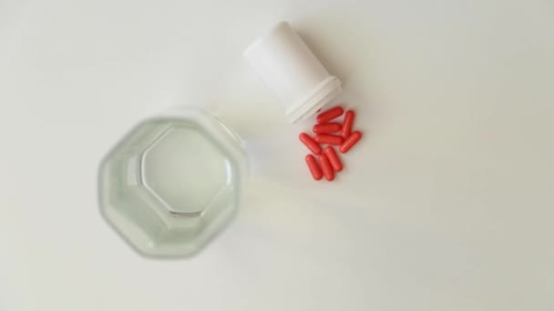 Cápsulas con un frasco blanco y un vaso de agua de pie sobre un fondo blanco, primero tomar un vaso, luego cápsulas. — Vídeo de stock