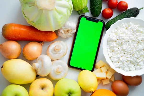 Meyve, sebze ve süt ürünleri arasında yeşil ekranlı bir telefon bulunuyor.