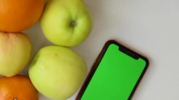 Telefonen med en grön skärm ligger på sidan av frukten och snurrar i en cirkel. — Stockvideo