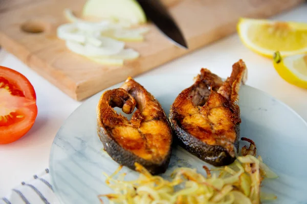 Soğanlı kızarmış balık bir tabakta, waffle havlusunda, yanında doğranmış soğan, limon ve domatesli bir kesme tahtası var..