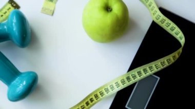 Yeşil bir elma, pullar, bir fitness elastik bant ve halterler daire şeklinde dönen bir mezura sarılır..
