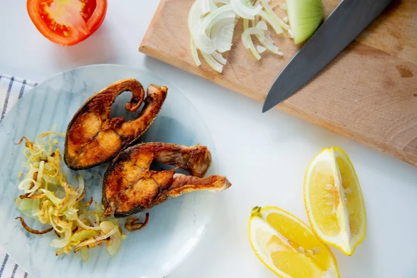 Soğanlı kızarmış balık bir tabakta, waffle havlusunda, yanında doğranmış soğan, limon ve domatesli bir kesme tahtası var..