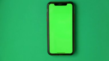 Kromakey ekranlı telefon yeşil bir arkaplanda duruyor, el periyodik olarak tıklamalar ve kaydırmalar yapıyor..