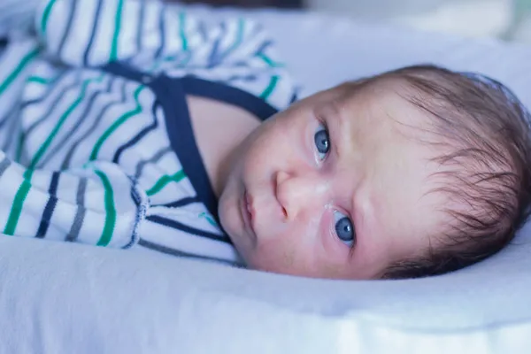 Un niño pequeño con un traje a rayas en serio y frunce el ceño mira a la cámara, acostado en una almohada blanca. — Foto de Stock