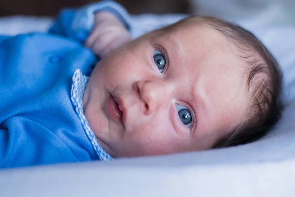 Un niño pequeño con ojos azules mira a la cámara con sorpresa frunciendo el ceño con una blusa azul — Foto de Stock