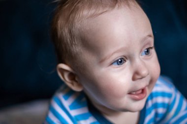 Çizgili tulumlu bir çocuk kameradan yüzünü çeviriyor ve gülümsüyor.. 