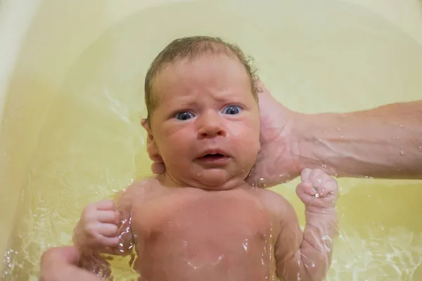 Un bebé recién nacido se está bañando en un baño por primera vez, su mano sostiene su cabeza, el bebé tiene miedo. — Foto de Stock