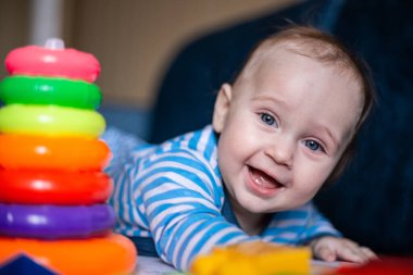 Çizgili takım elbiseli küçük bir çocuk karnının üstünde yatıyor, yanında bir çocuk piramidi ve oyuncakları var..