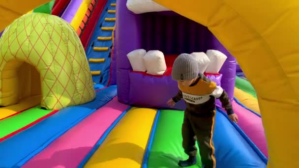 Novorossiysk, 01.11.2021. Um garotinho de terno e chapéu pula em um trampolim multicolorido e cai no final. — Vídeo de Stock