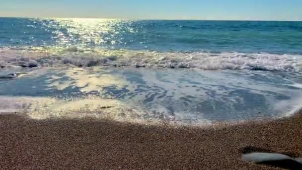 Blaues Meer und blaue Wolken, eine weiße Welle plätschert am Ufer und spült den Strand mit feinem Steinsand. Befriedung — Stockvideo