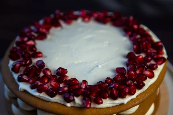 Торт с губчатыми тортами, украшенный белым кремом и семенами граната сверху в круге, слои крема видны кругами сбоку, вид сбоку крупным планом — стоковое фото