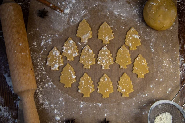 반죽에서 떼어 낸 많은 쿠키들은 크리스마스 트리의 형태로 밀가루로 빵을 굽는 종이 위에 놓여 있습니다. — 스톡 사진