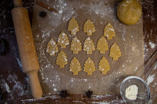 반죽에서 떼어 낸 많은 쿠키들은 크리스마스 트리의 형태로 밀가루로 빵을 굽는 종이 위에 놓여 있습니다. — 스톡 사진