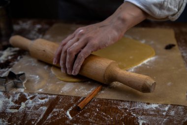 Hamur, parşömen üzerinde bir oklavayla sarılmış, un etrafa saçılmış, fotoğraf koyu bir anahtarın içinde.