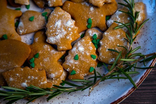 Les biscuits sont sur une assiette de différentes formes, au premier plan il y a un biscuit sous la forme d'un arbre de Noël, décoré avec du sucre en poudre comme la neige et de petits arbres de Noël verts contre le — Photo
