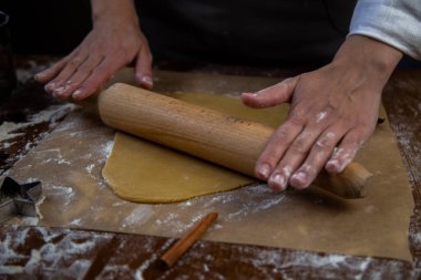 Hamur, parşömen üzerinde bir oklavayla sarılmış, un etrafa saçılmış, fotoğraf koyu bir anahtarın içinde.