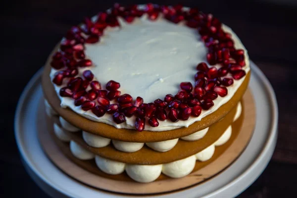 Pastel con pasteles de esponja, decorado con crema blanca y semillas de granada en la parte superior en un círculo, capas de crema son visibles en círculos en el lado, una vista de cerca desde el lado — Foto de Stock