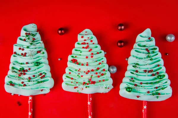 Três árvores de Natal turquesa feitas de bizet em paus espalhados com bolas de pó coloridas em um fundo vermelho brilhante, bolas vermelhas e prateadas se encontram ao lado umas das outras. — Fotografia de Stock