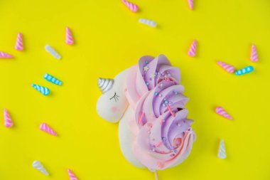 Pembe-mor kuyruklu beyaz bir tek boynuzlu at ve parlak sarı bir arka planda uzanan gümüş bir boynuz. Etrafına çok renkli boynuzlar saçılmış..