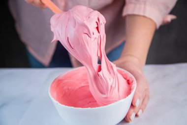 Pembe kremalı marangoz, beyaz mermer arka planda beyaz bir kasede bir pasta şefinin elleriyle karıştırılır.